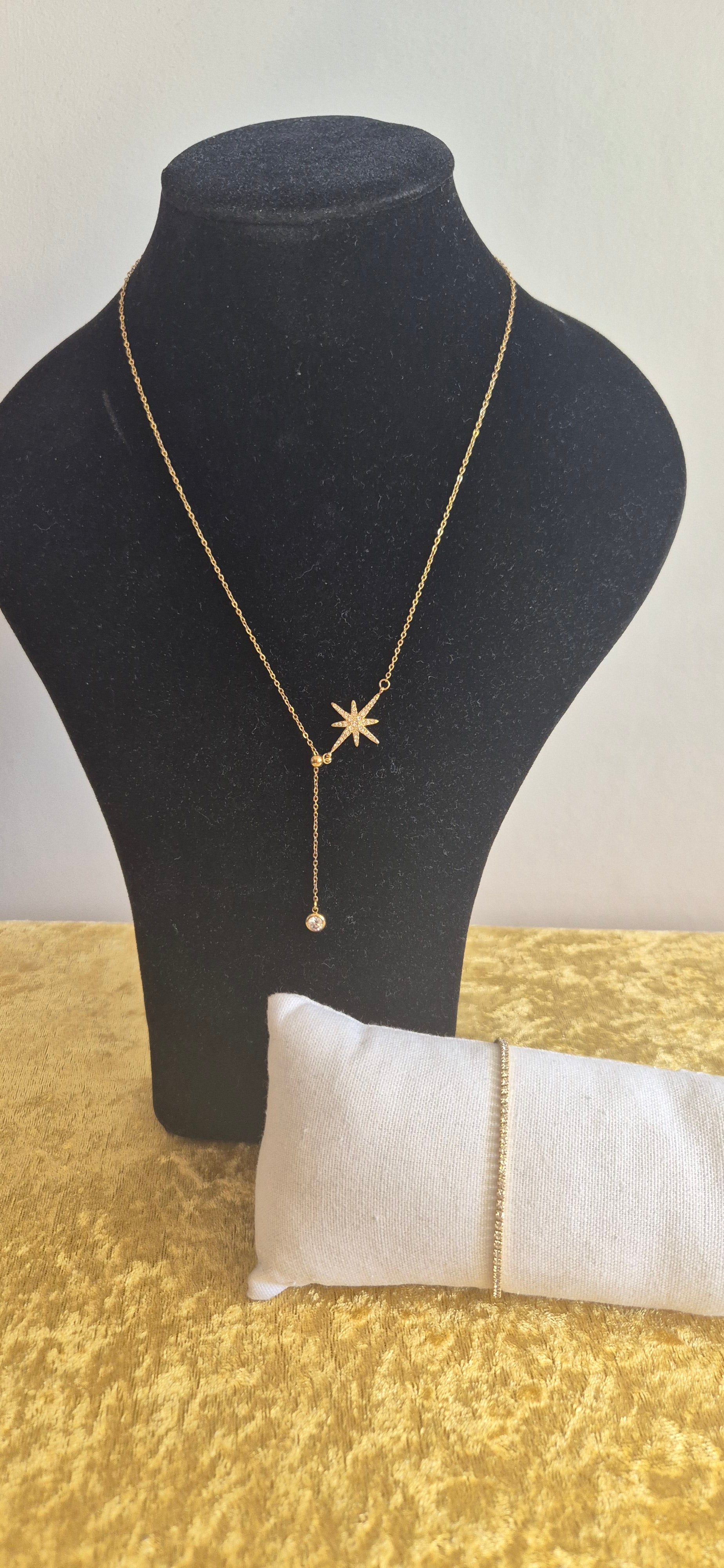 Nordic Glow Set Guld – Nordstjärnan halsband på svart display och Isälv Tennisarmband på vit kudde med guldigt underlag